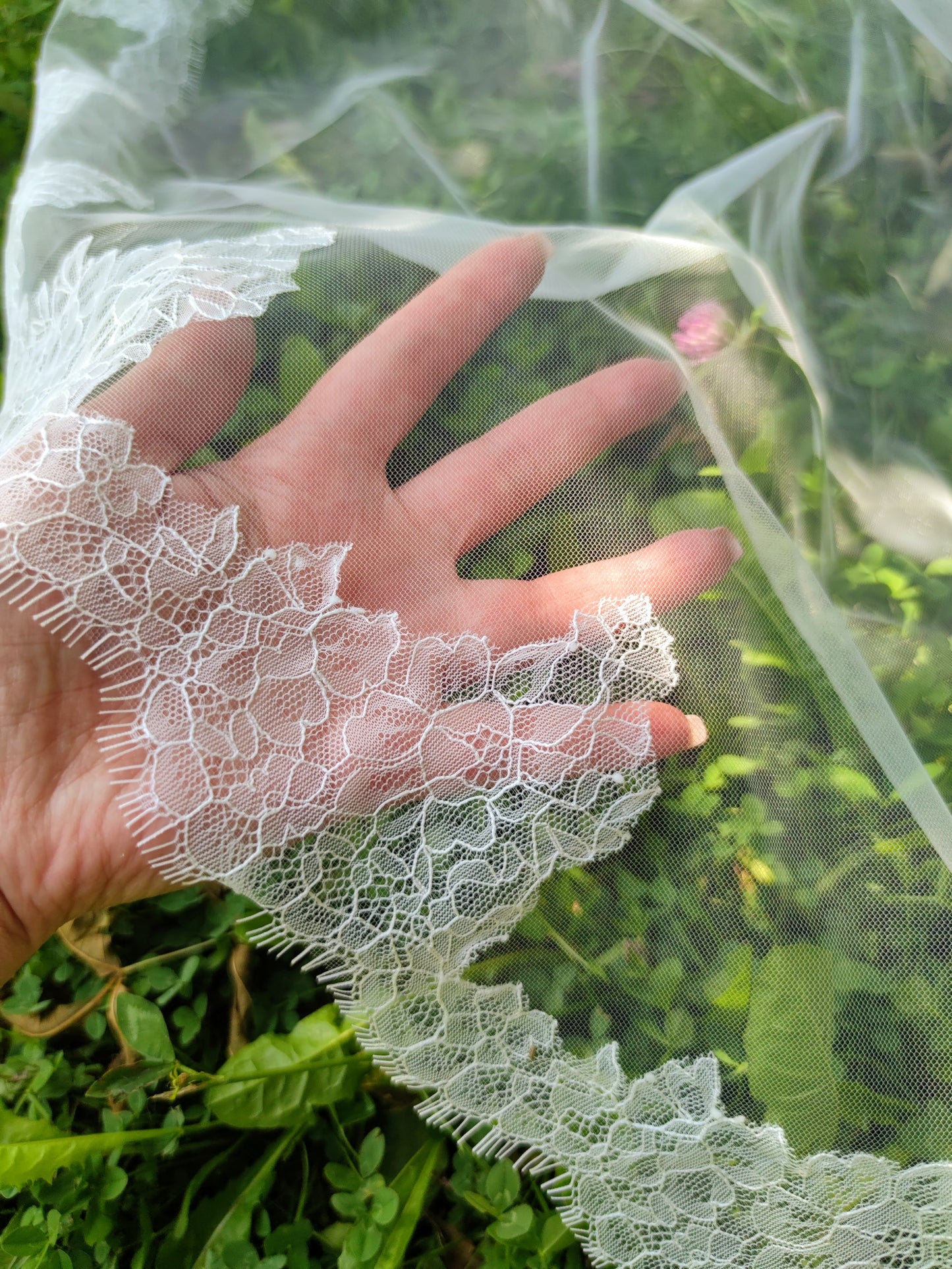 Close-up of a hand holding the scalloped floral Chantilly lace edge and dotted tulle of The Laima mantilla veil