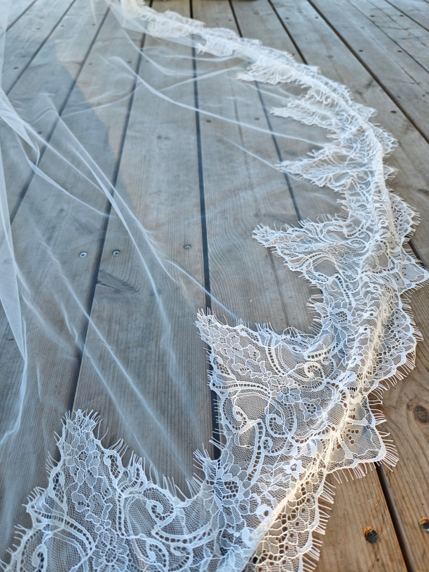 Hand-sewn Chantilly lace trim on main layer of two-tier ivory wedding veil, intricate floral French lace border