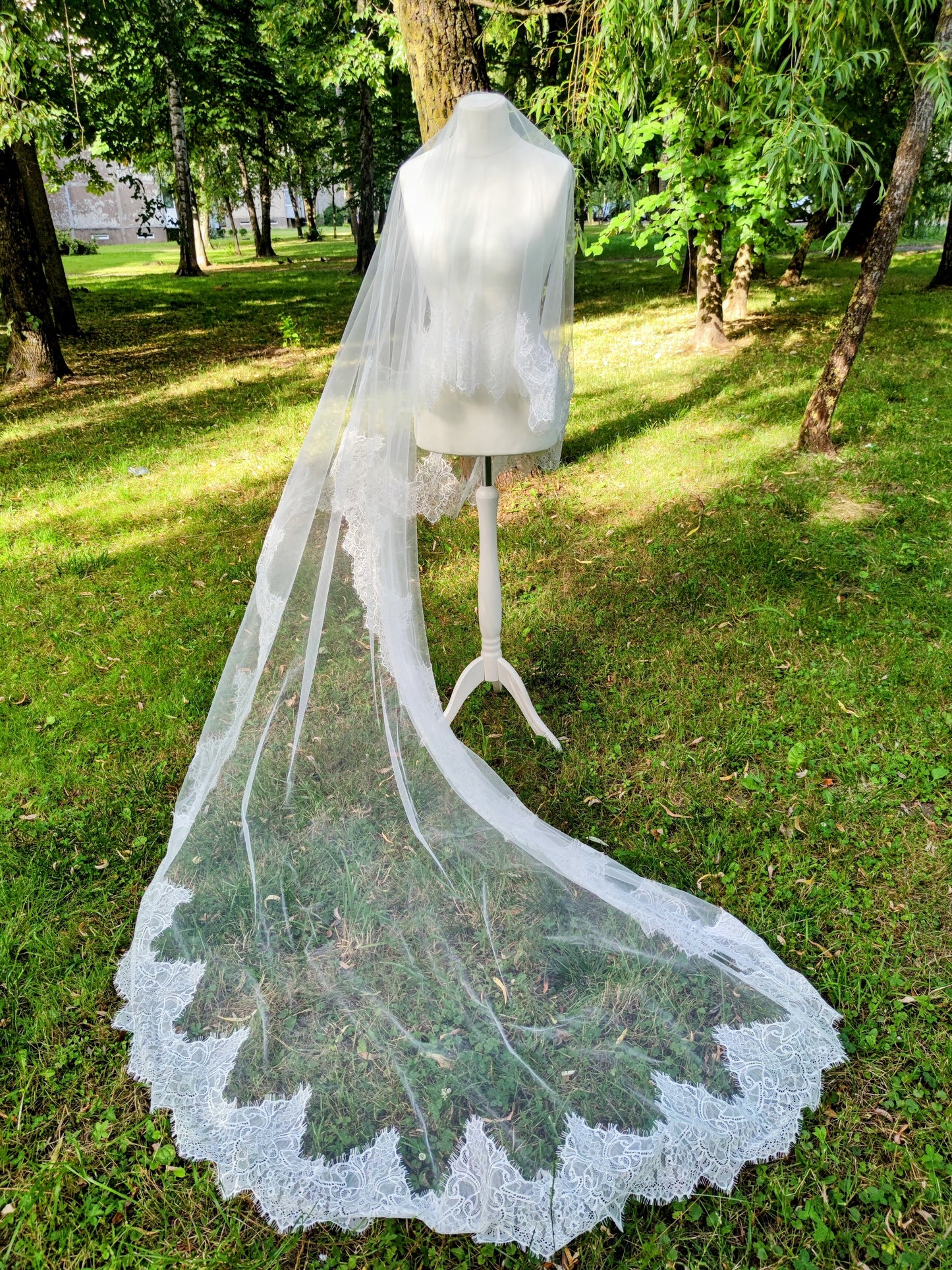 Chantilly lace Cathedral veil with blusher on display in a lush green outdoor setting