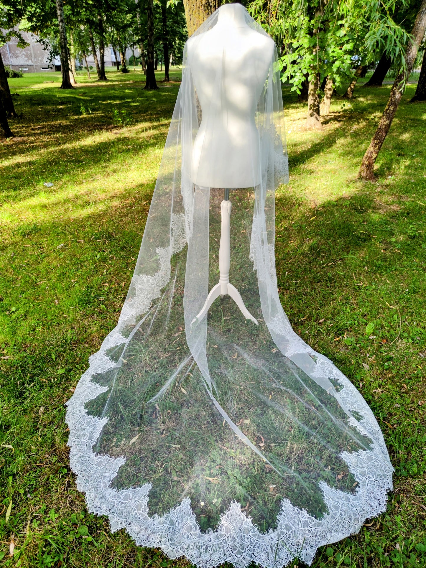 Chantilly lace mantilla Cathedral veil with blusher displayed on mannequin in outdoor garden setting.