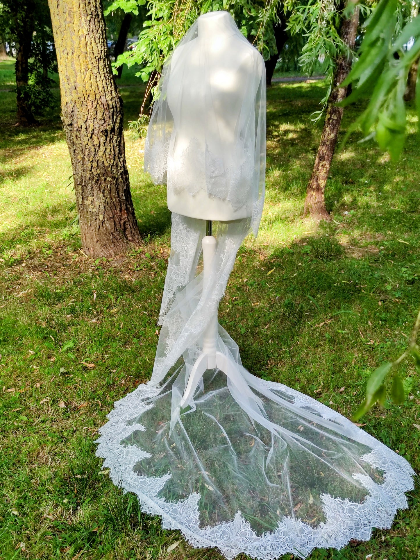 Chantilly lace Cathedral veil with blusher draped on mannequin in outdoor garden setting