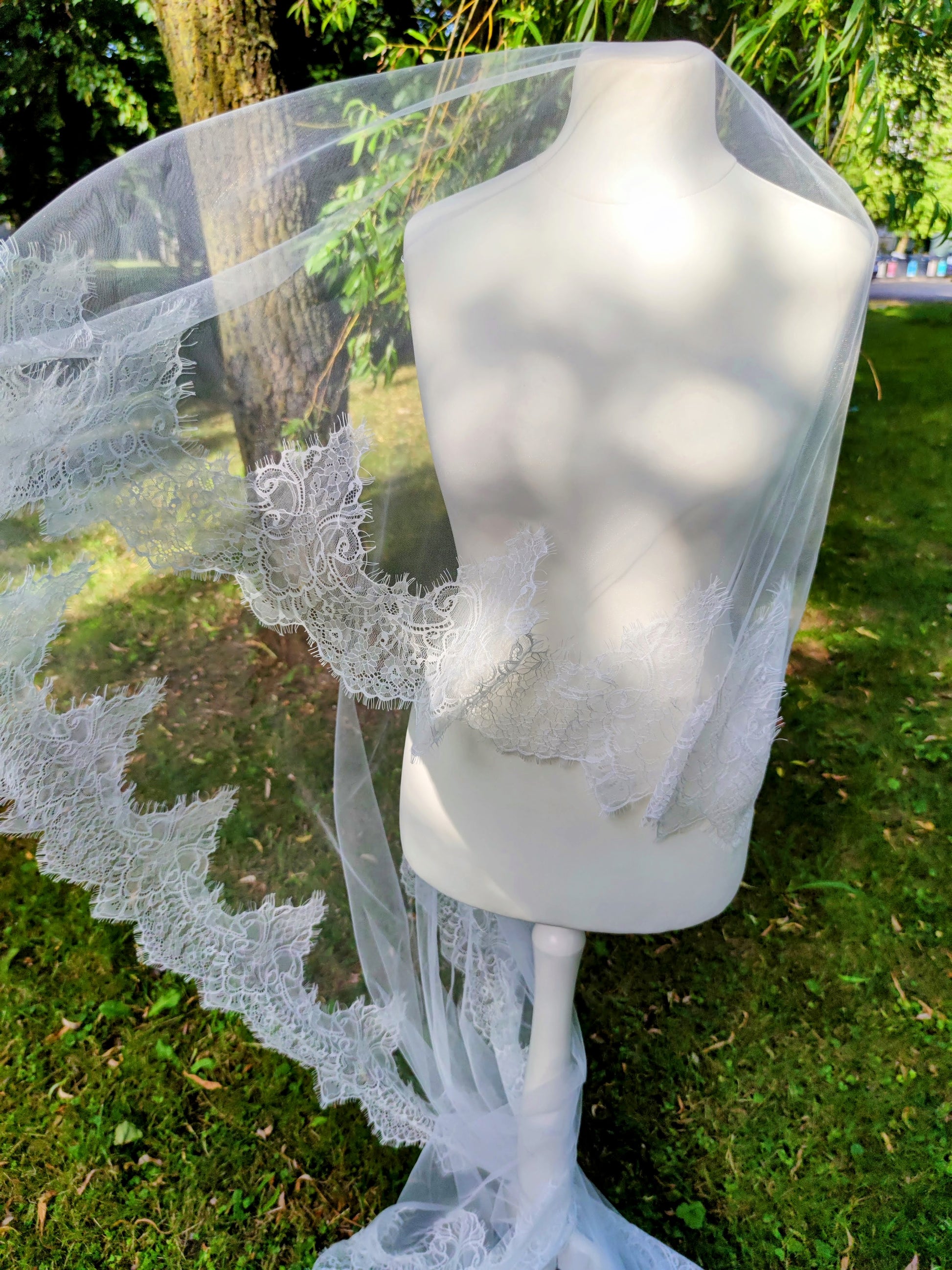 Chantilly lace mantilla veil with blusher displayed in outdoor setting on mannequin