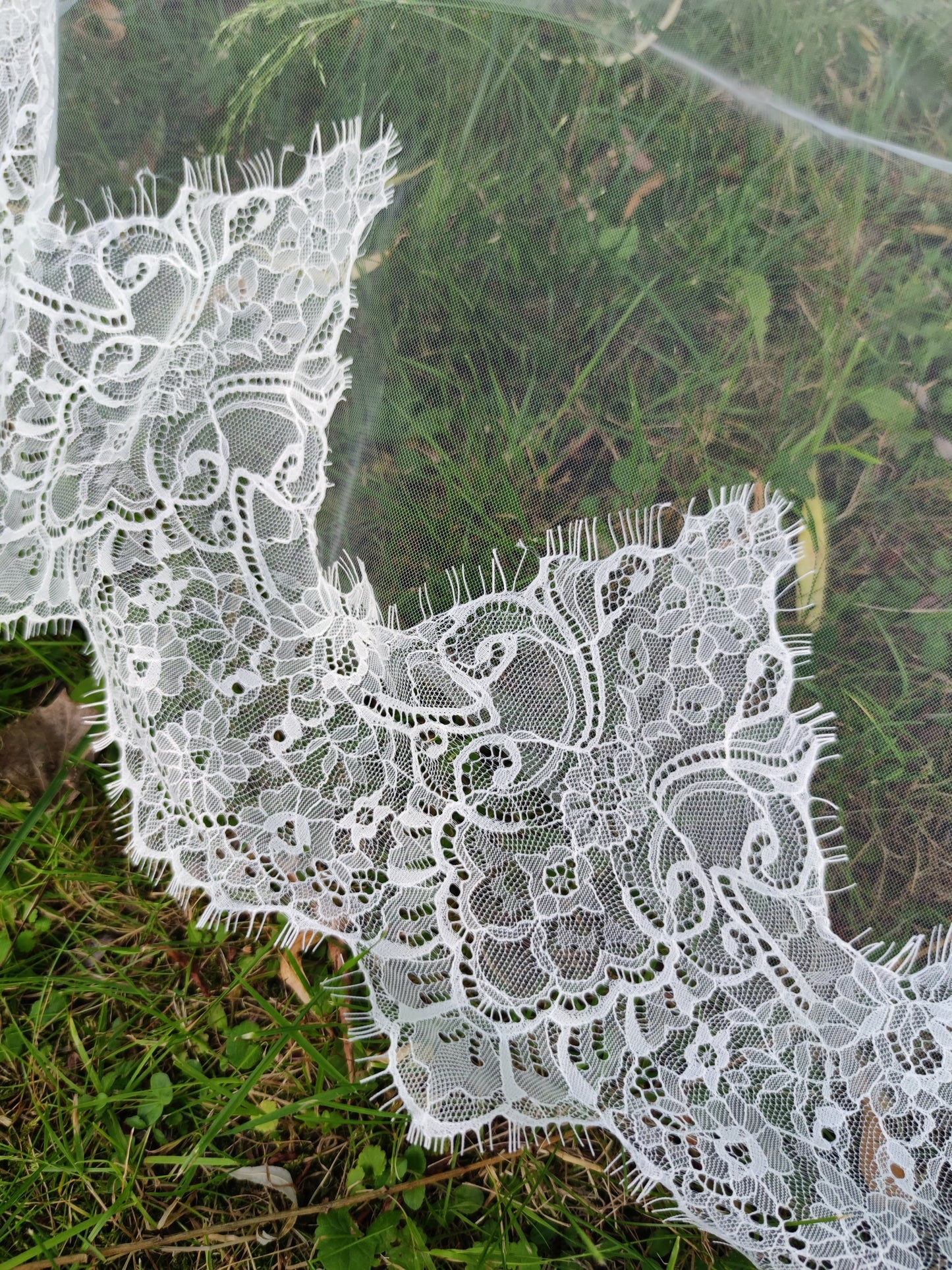 Close-up of Chantilly lace mantilla veil on grass showing intricate French lace craftsmanship in light ivory