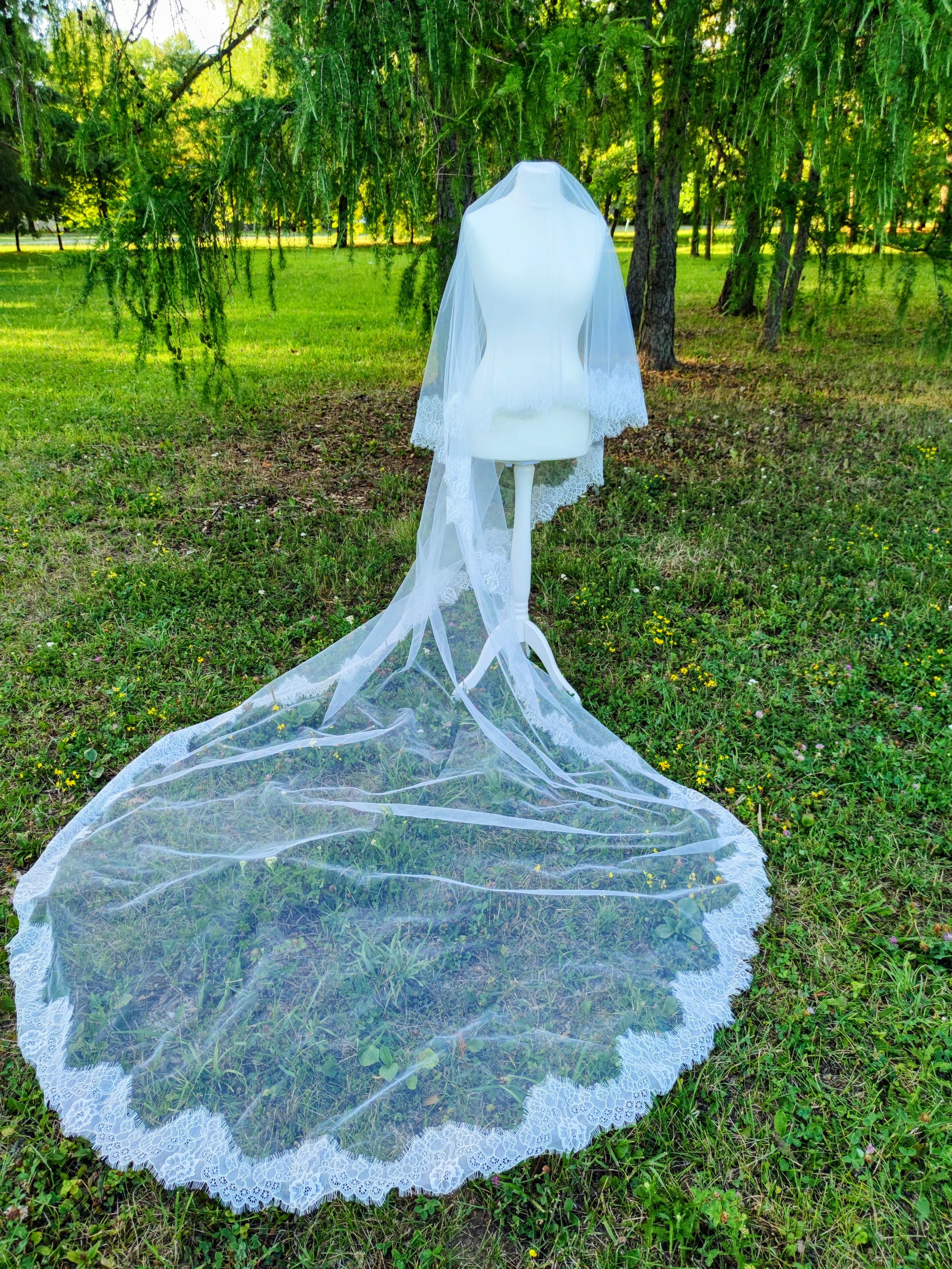 Chantilly lace Cathedral veil with blusher in light ivory displayed on mannequin outdoors.