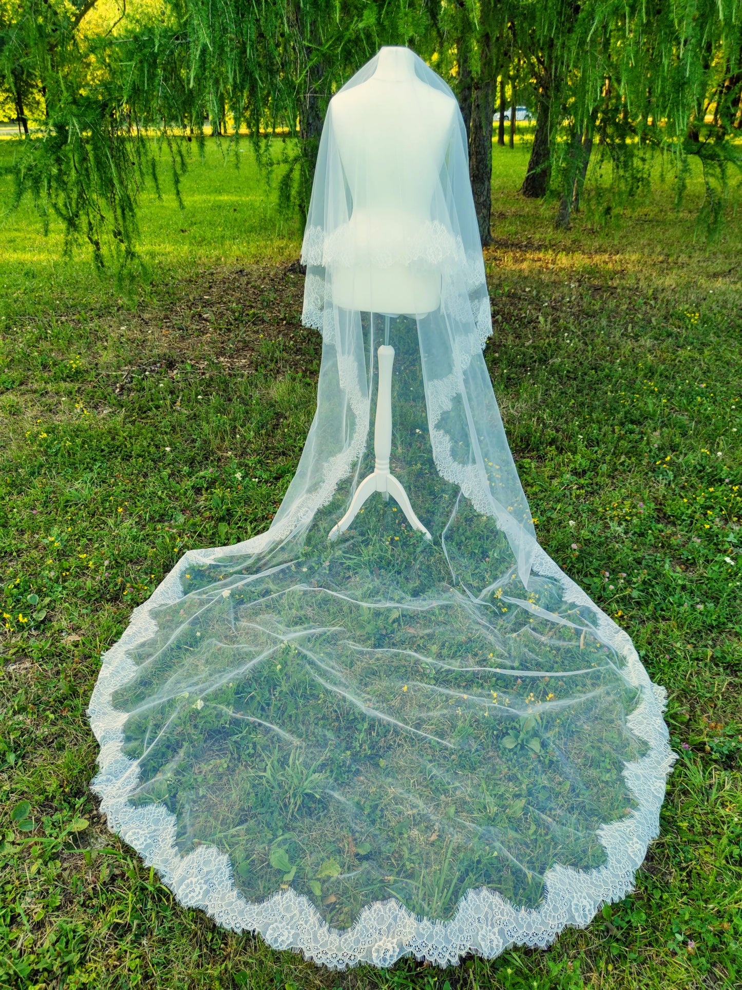 Chantilly lace Cathedral veil with blusher in light Ivory, 320 cm long with hand-sewn delicate lace, displayed outdoors on a mannequin.