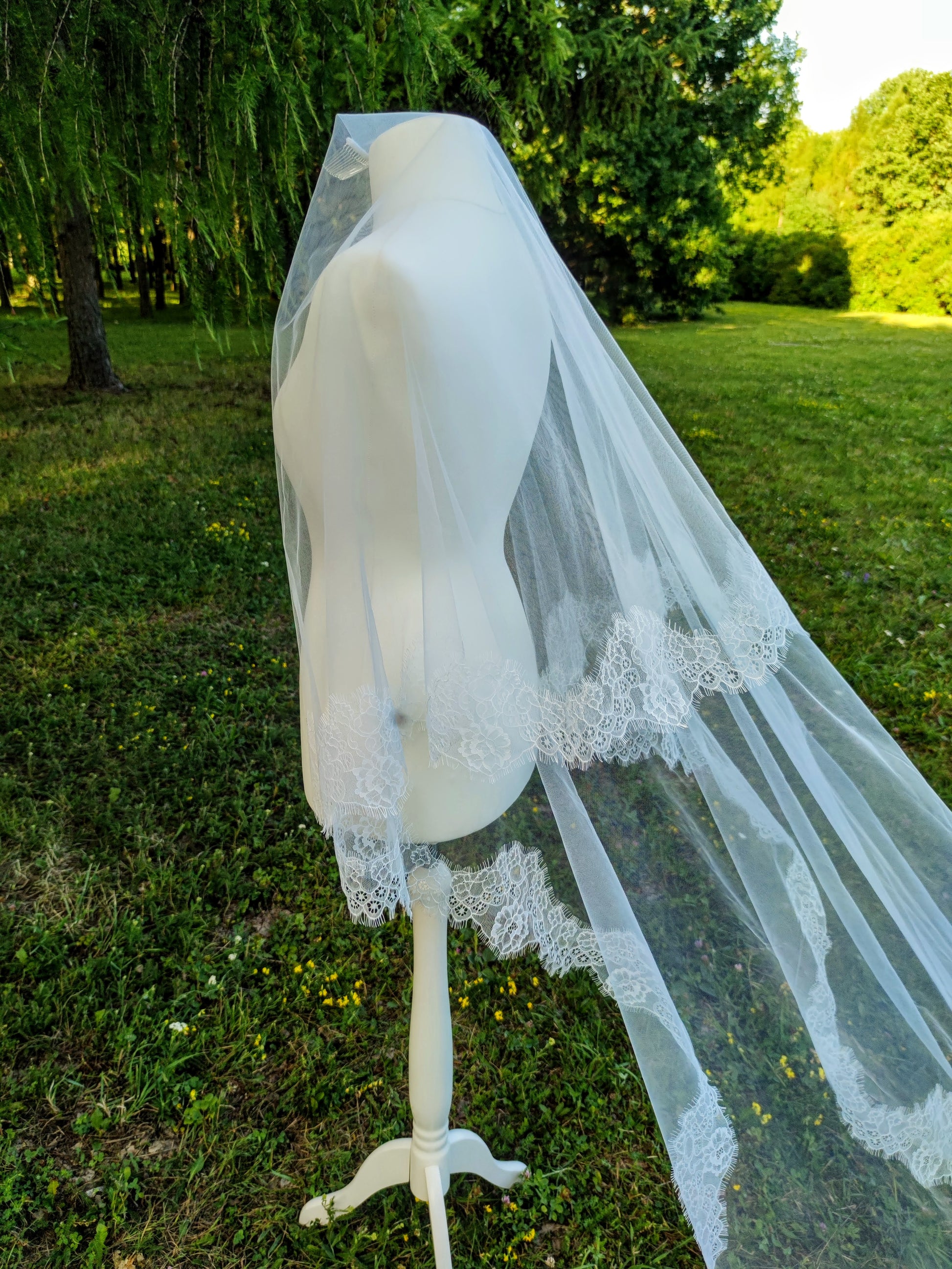 Light ivory Chantilly lace Cathedral veil with blusher displayed on mannequin in outdoor setting