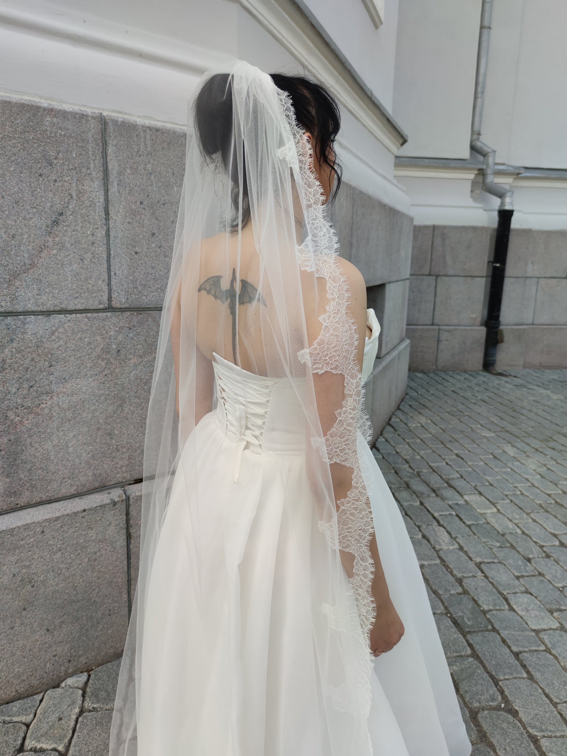 Light ivory one-tier wedding veil with Chantilly lace trim, attached to a metal comb, back view