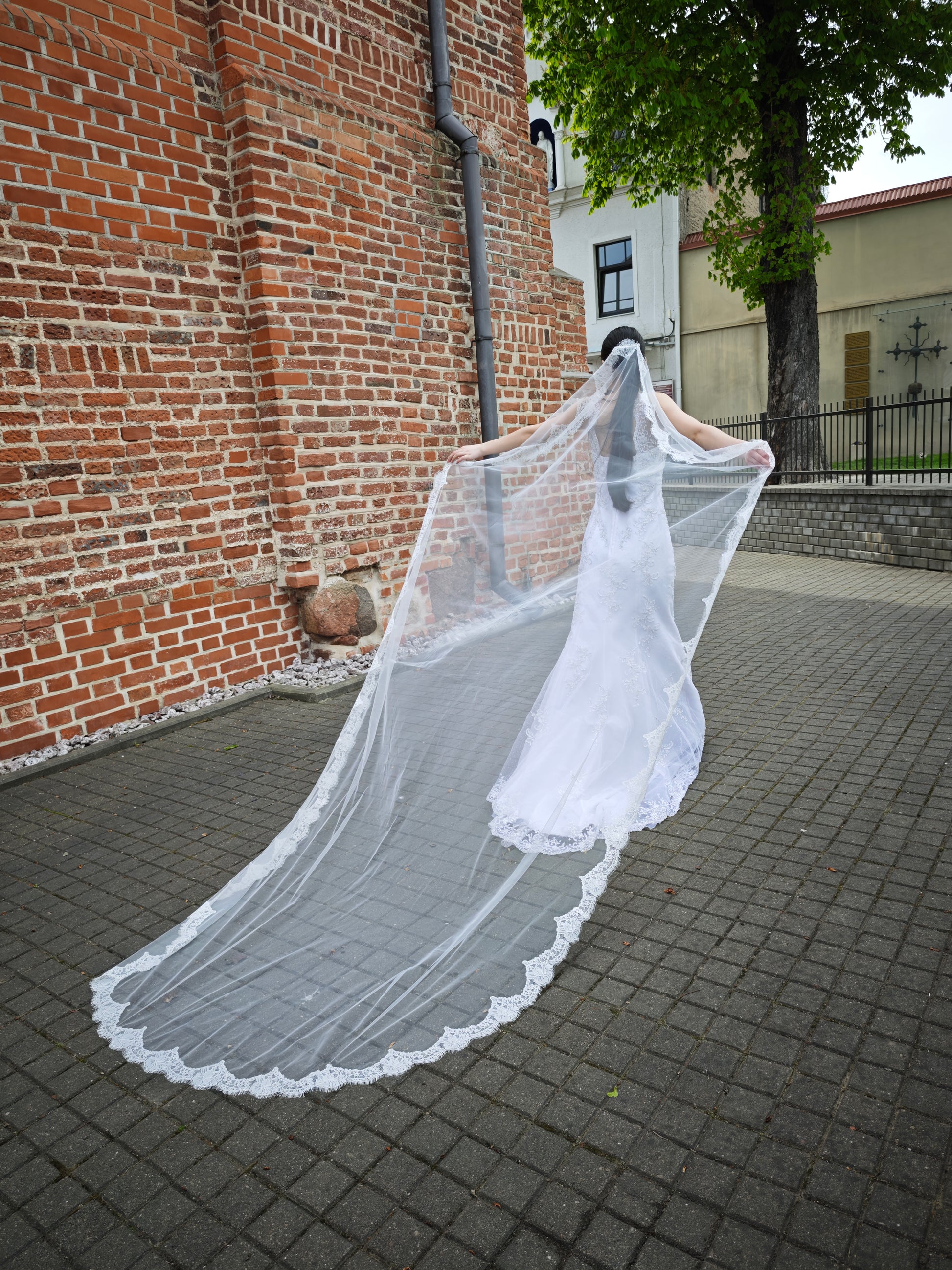 Handcrafted ivory Chantilly lace mantilla veil with full perimeter lace edge, side view, bride at historic brick arch