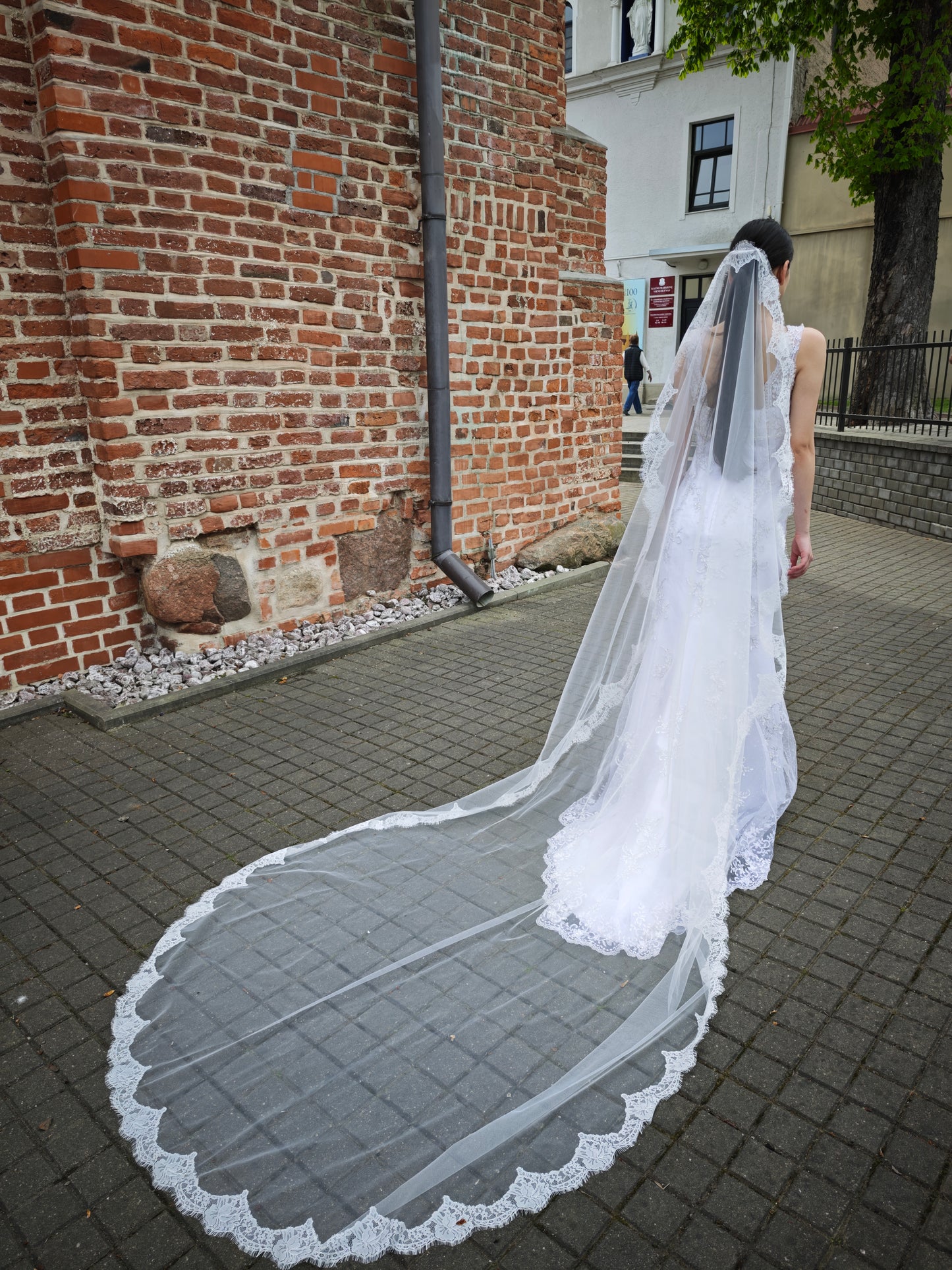 Long ivory mantilla veil with scalloped Chantilly lace border trailing along cobblestone, full perimeter lace visible