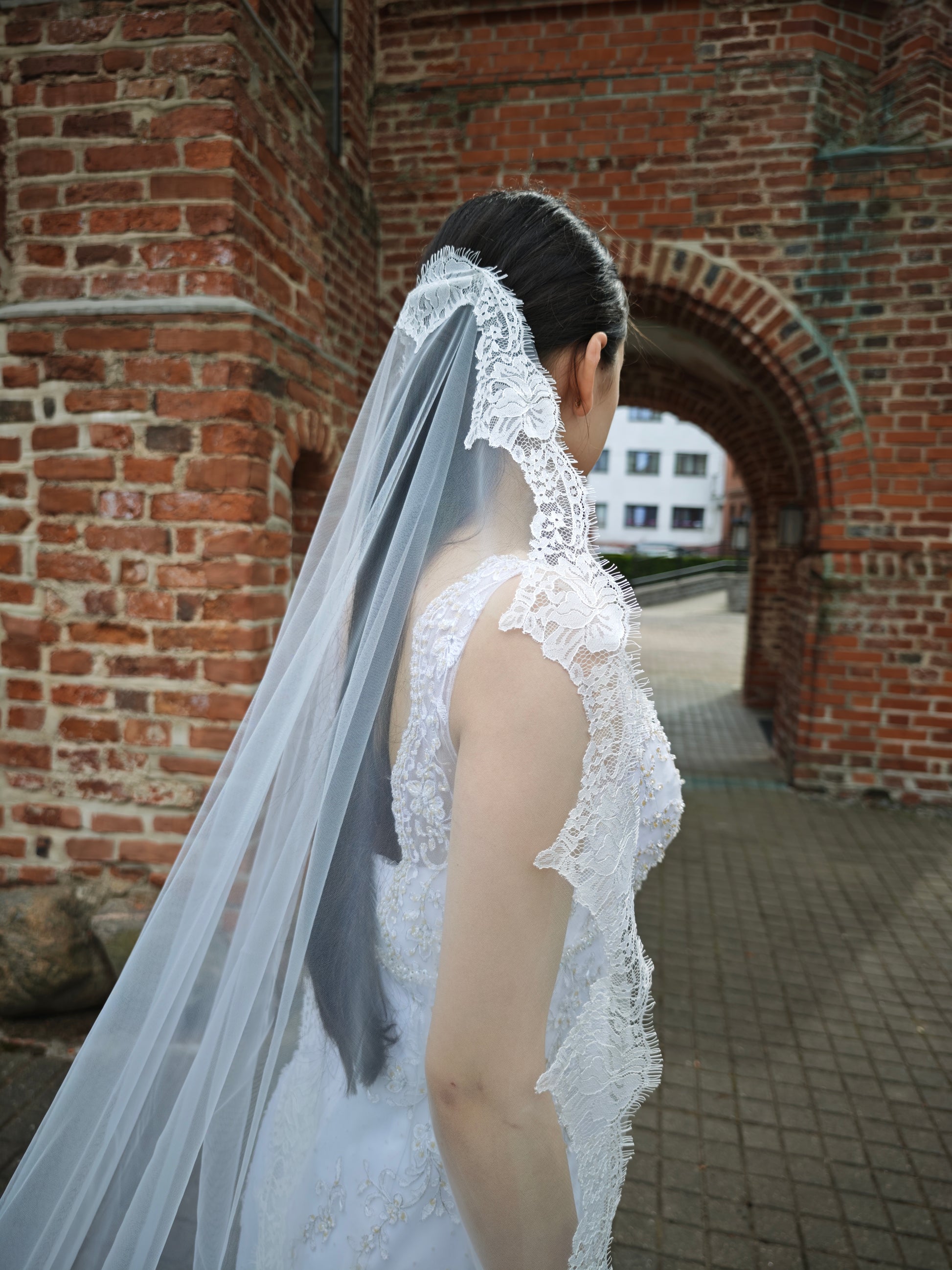 Spanish mantilla wedding veil with wide Chantilly lace border, bride at historic brick church, Kaunas, Lithuania