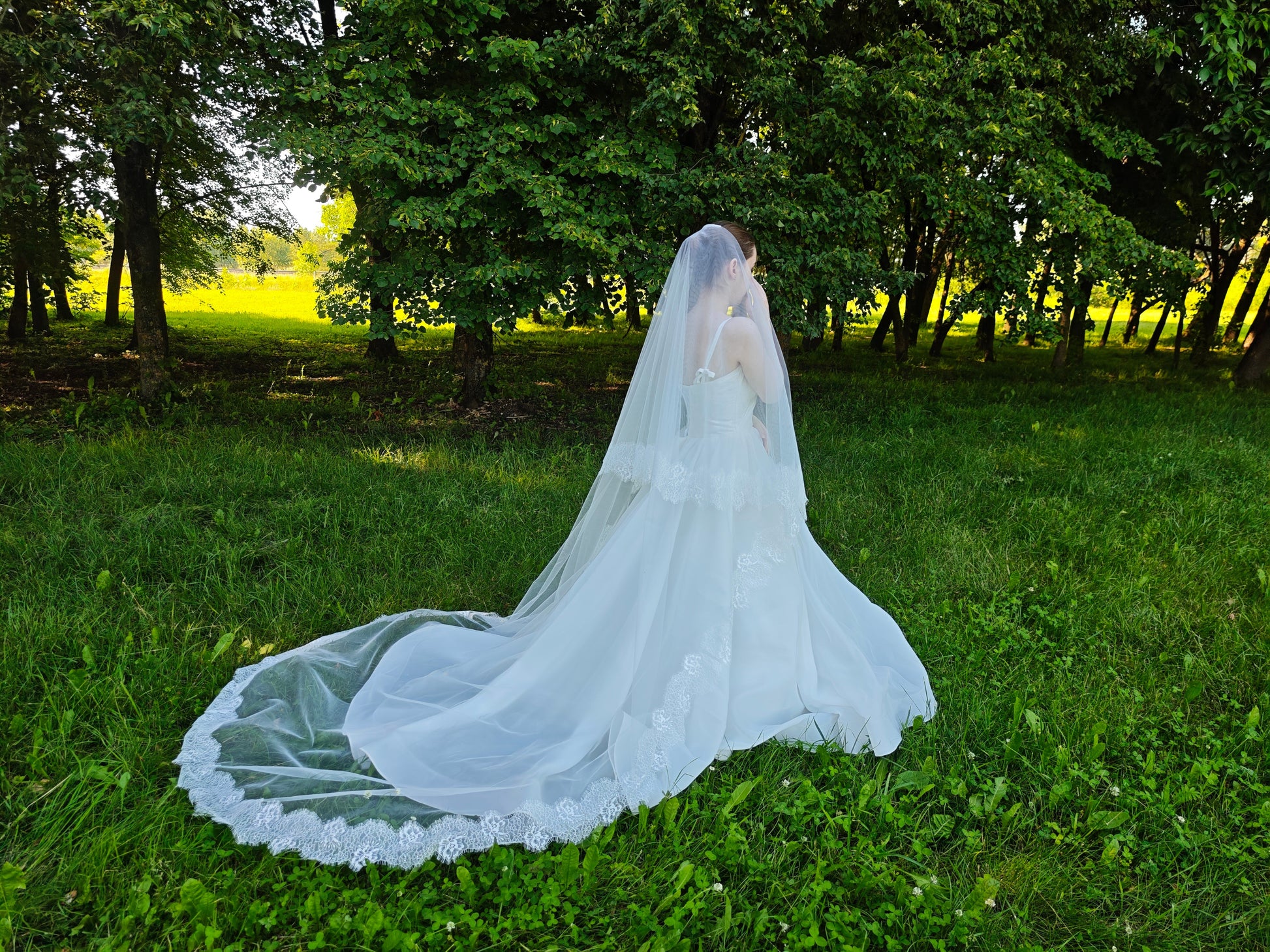 Royal length two-tier wedding veil with floral lace trim, ivory tulle train spread across the grass in a forest clearing