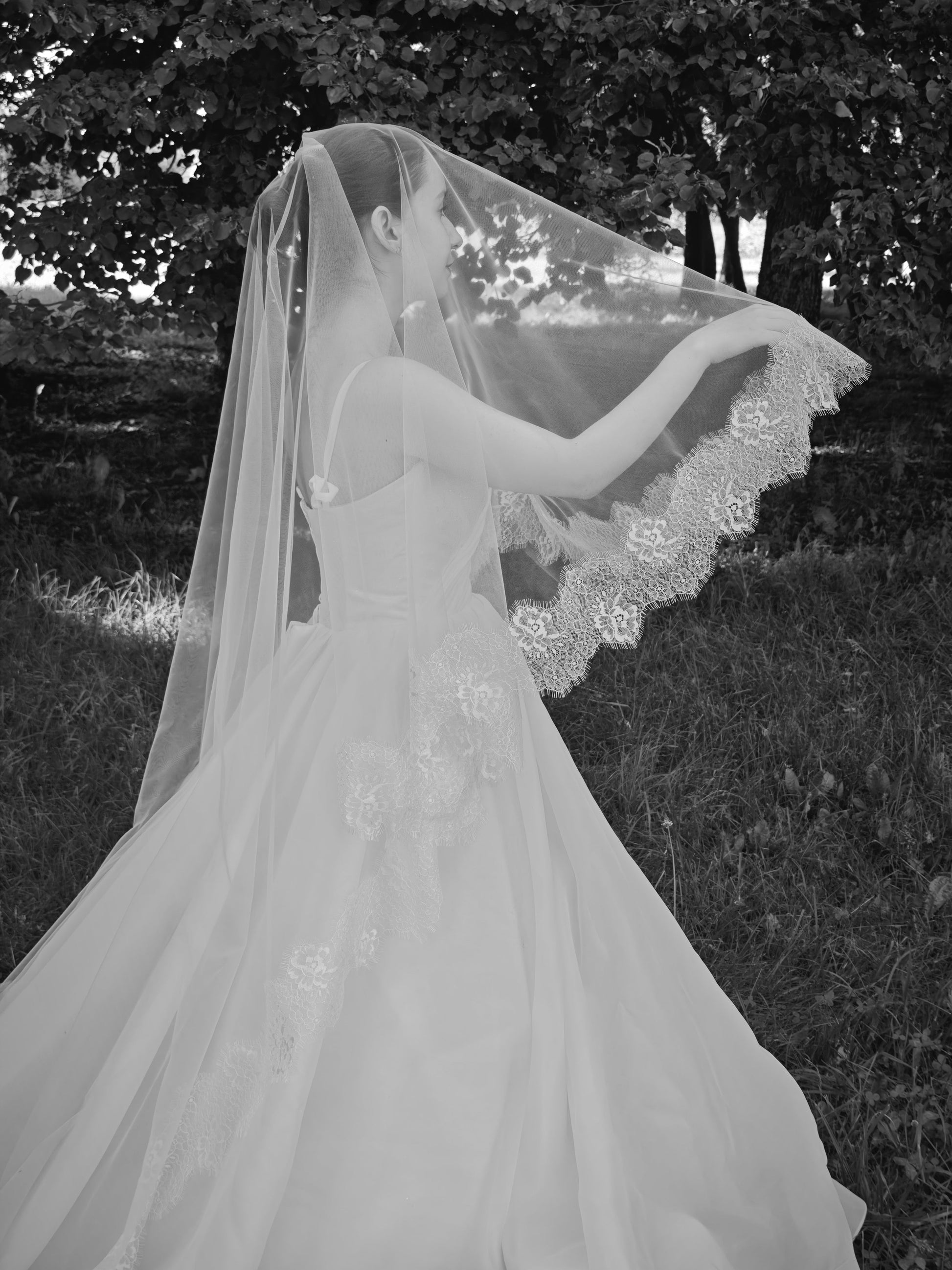 Two-tier ivory wedding veil with blusher lifted over the face, floral Chantilly lace hand-sewn edge, forest bridal portrait