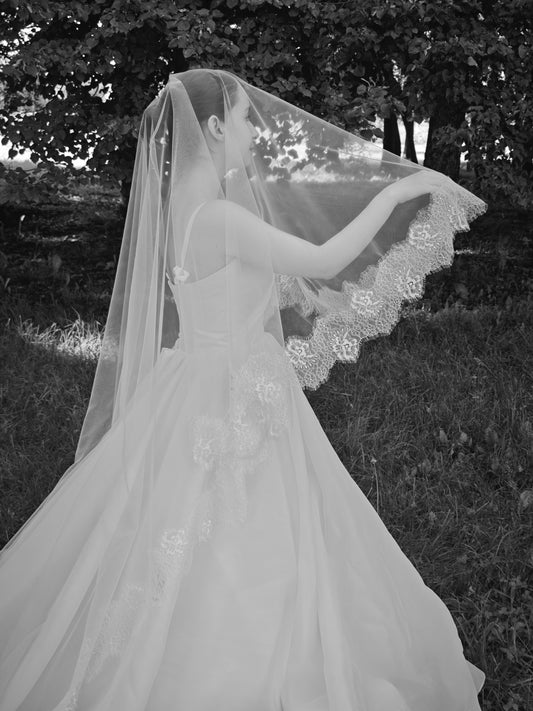 Two-tier ivory wedding veil with blusher lifted over the face, floral Chantilly lace hand-sewn edge, forest bridal portrait