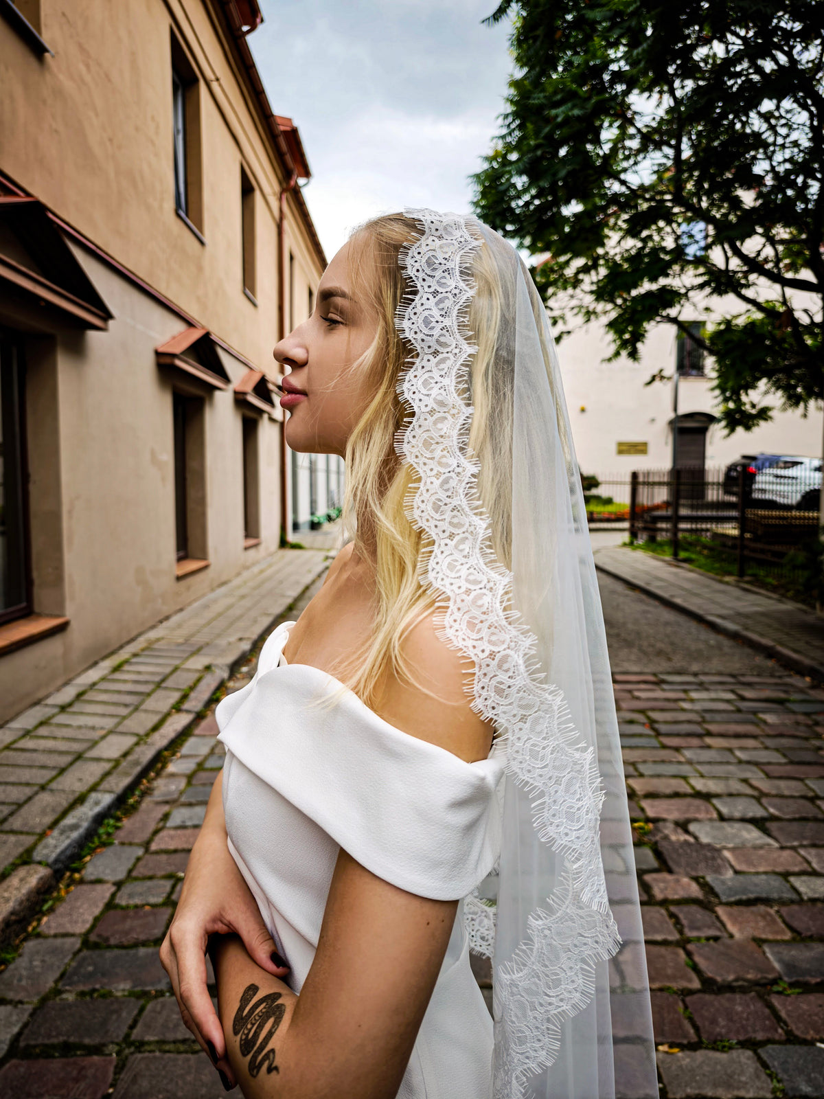 Simple lace mantilla veil with narrow Chantilly lace edge, side view of bride on a cobblestone street