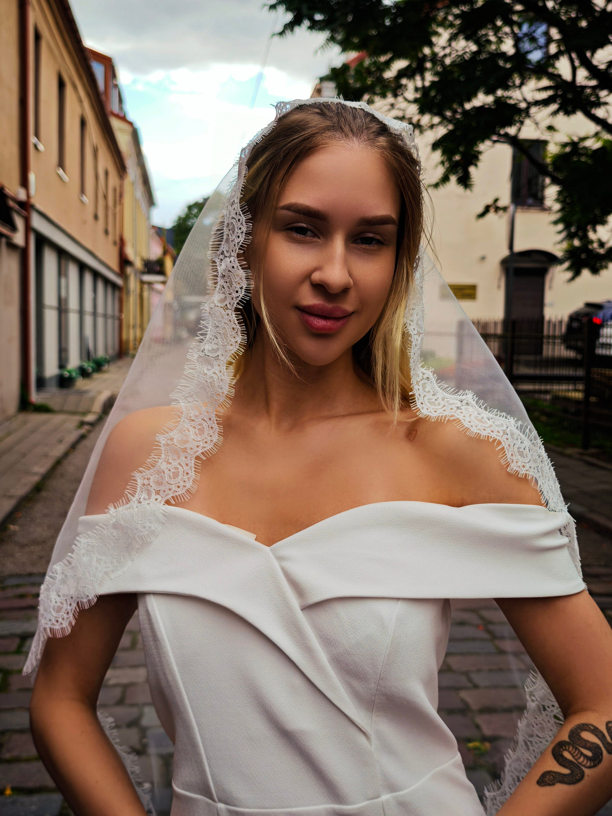 Bride in an off-shoulder dress wearing a lace mantilla veil, narrow Chantilly lace edge framing the face