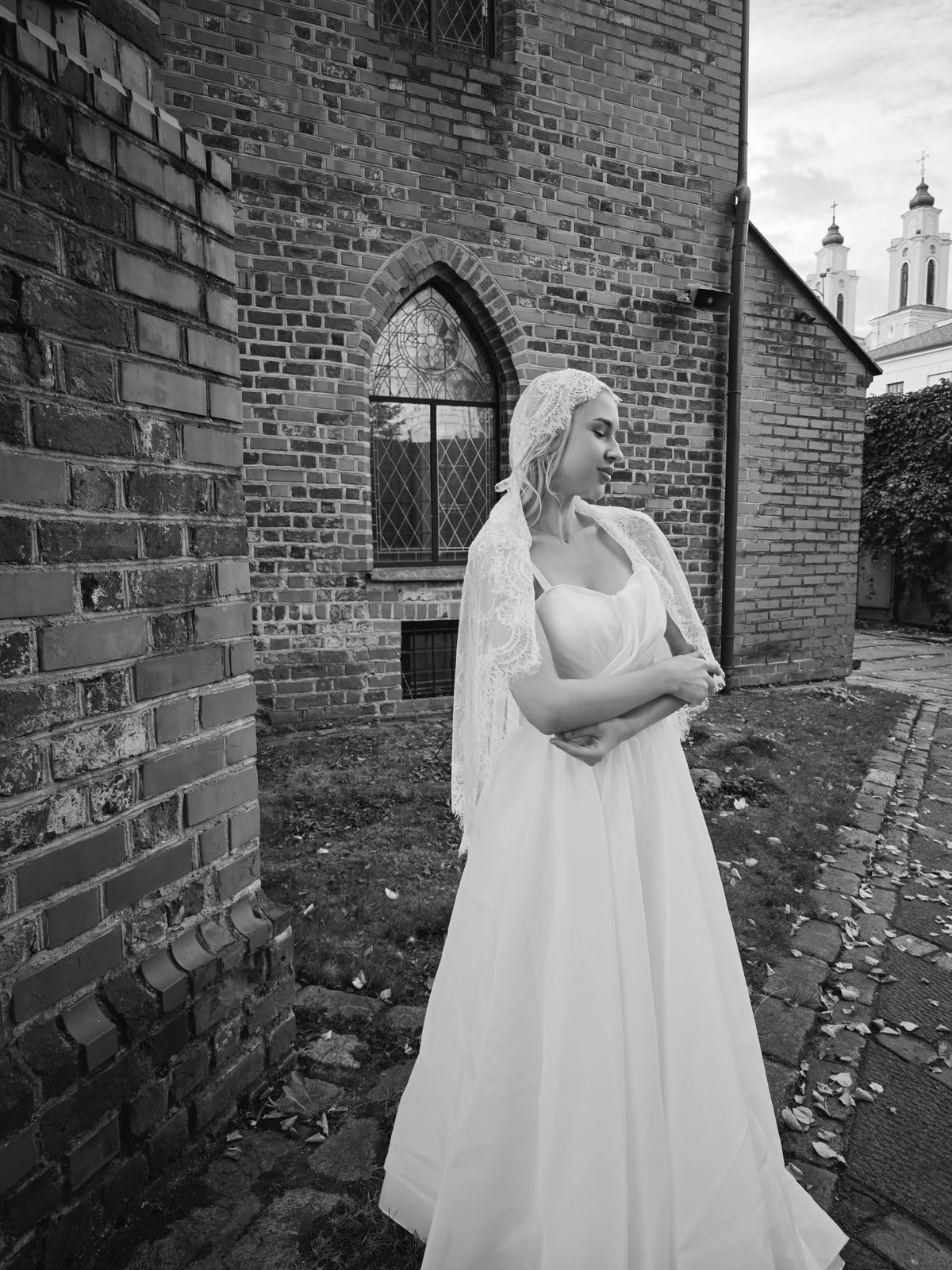Ivory lace cap veil framing the bride's head, black and white portrait by an old brick church