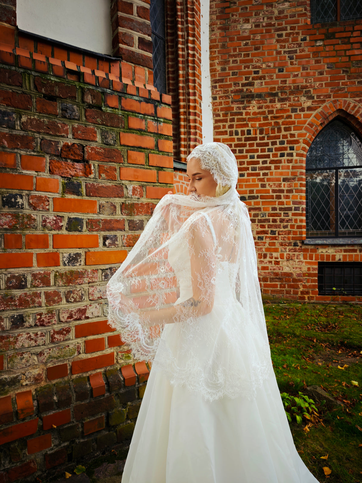 Bride lifting the scalloped lace edge of a full lace Juliet cap veil, side view, ivory wedding dress