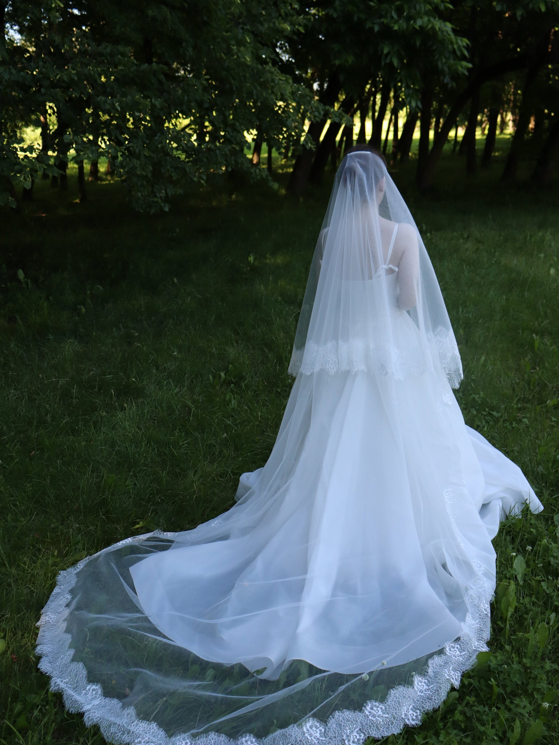Floral Chantilly lace bridal veil at dusk, two-tier ivory tulle with a lace-edged train trailing on the lawn