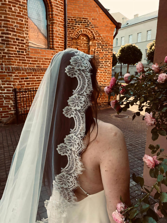 Light ivory mantilla wedding veil with Chantilly lace trim worn by bride, back view